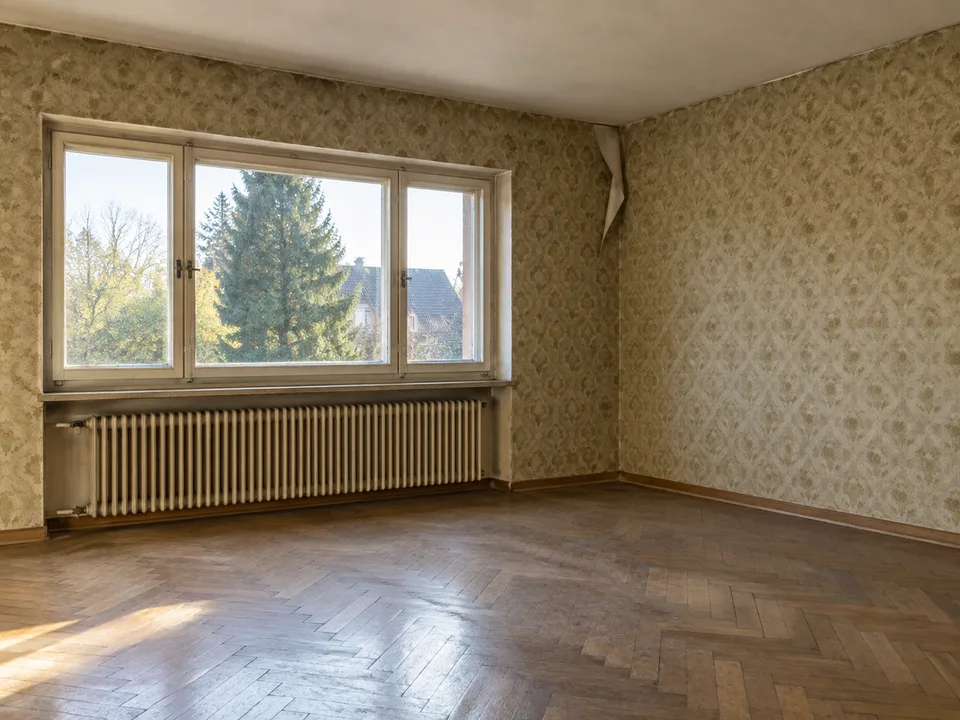 Leeres älteres Wohnzimmer mit abgenutztem Parkett und stellenweise gelöster Tapete; KI-generiertes Beispiel.